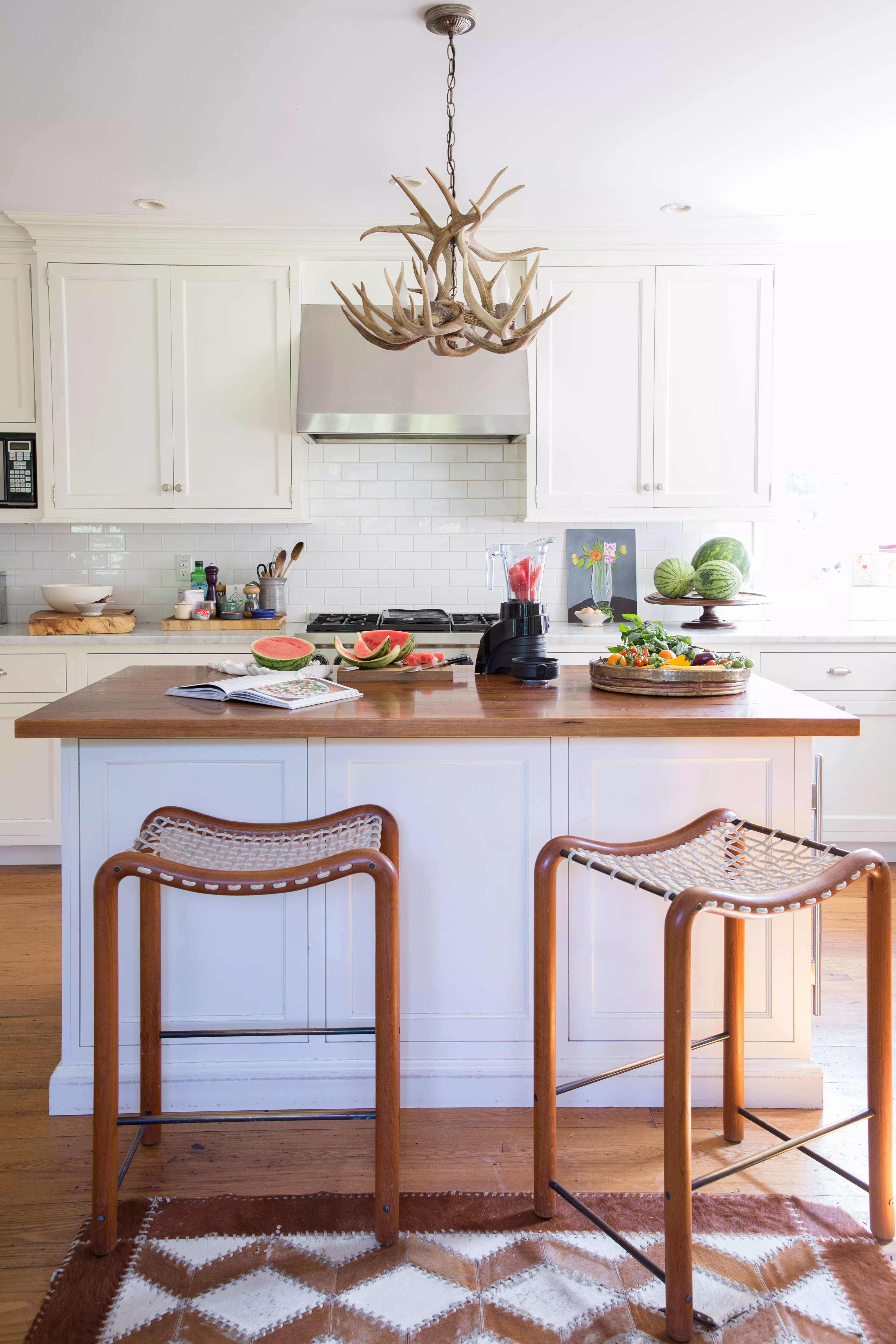 McGinnis white kitchen with walnut island, rope-seat stools and antler chandelier; Stools by kitchen island
